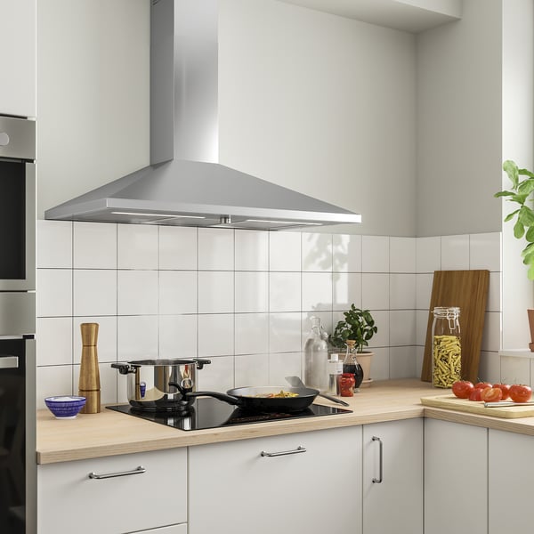 Modern kitchen featuring RYTMISK stainless steel hood, white cabinets, wooden countertop, and cooktop with black pan.
