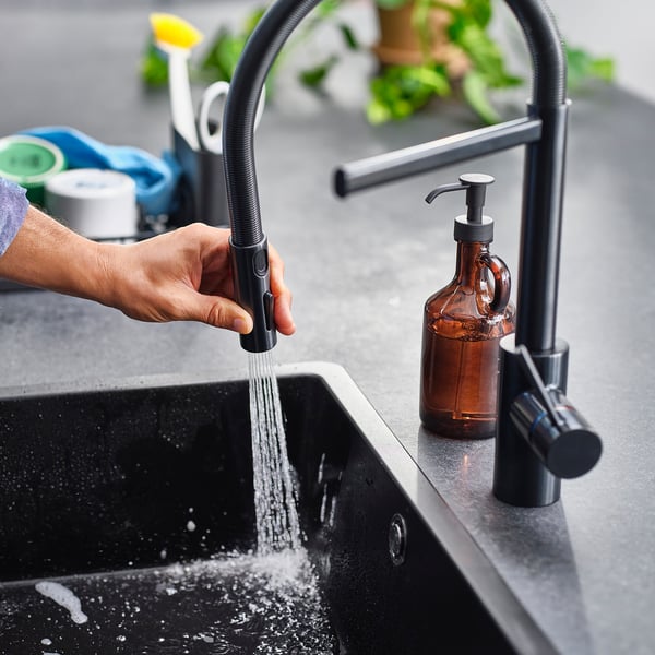 Hand holds kitchen tap spray head, water flowing into sink.
