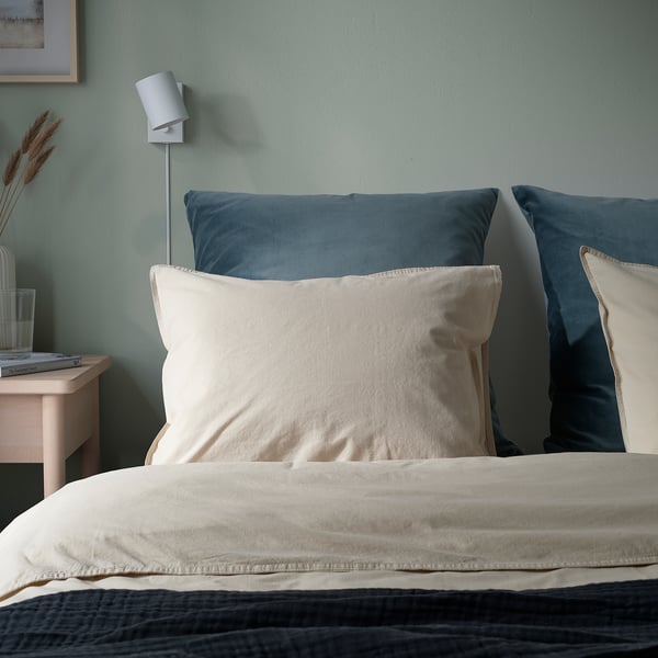 Cosy bedroom with beige cushion, blue pillows, green wall, lamp, books, vase.