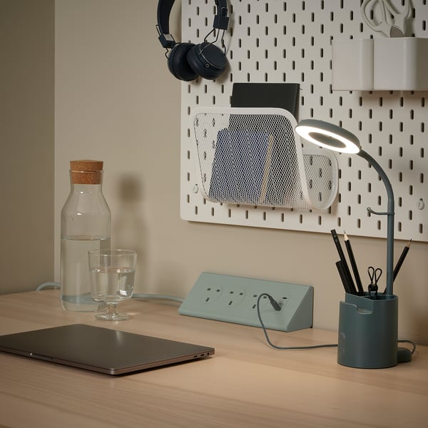 Modern desk setup with SKOTAT extension cord, laptop, lamp, and office supplies on a pegboard.