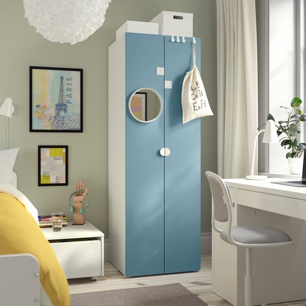 Blue SMÅSTAD wardrobe towers near white desk and chair. Room includes bed with yellow pillows, art, rug.