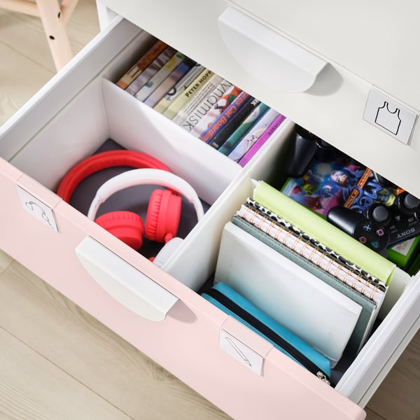 Three pink and white drawers open to reveal items: red headphones, books, video games, and notebooks. Organised, spacious, and stylish.