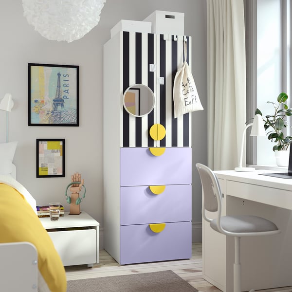 Modern bedroom with striped wardrobe, purple drawers, circular mirror, desk, art, and bedside table with headphones and books.