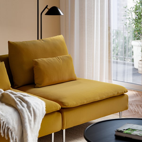Mustard yellow sofa near window, lamp behind, book on table.