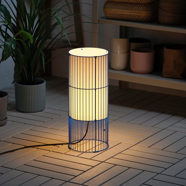 Modern lamp on wooden deck. Illuminates warm light. Stands upright, suitable for indoors/outdoors.