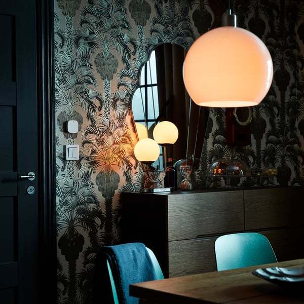 Modern dining area featuring teal chairs, black sideboard, white globe light fixture, and botanical wallpaper.