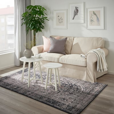 Living room with beige sofa, rug, table, and plant.
