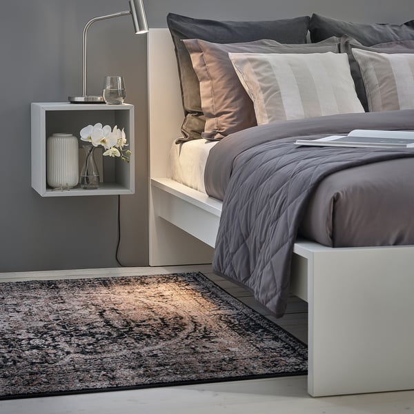 Modern bedroom with grey bedding, white orchids, and a grey rug.