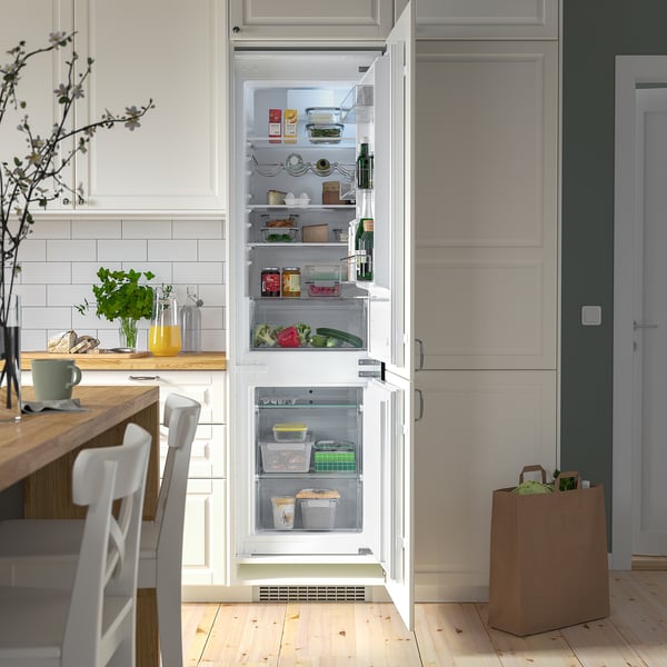 Open kitchen cabinet revealing a well-organized fridge with adjustable shelves, holding various food containers and bottles.