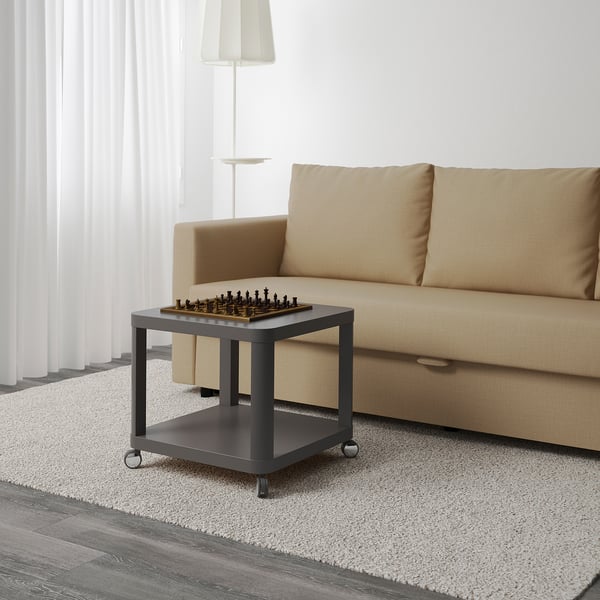 Small, movable coffee table with wheels, holding a chess set, ideal for multi-purpose rooms.