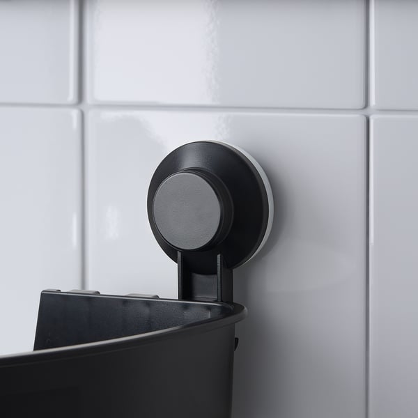 Black suction-mounted corner shelf in bathroom. Holds shampoo bottles, drains water.