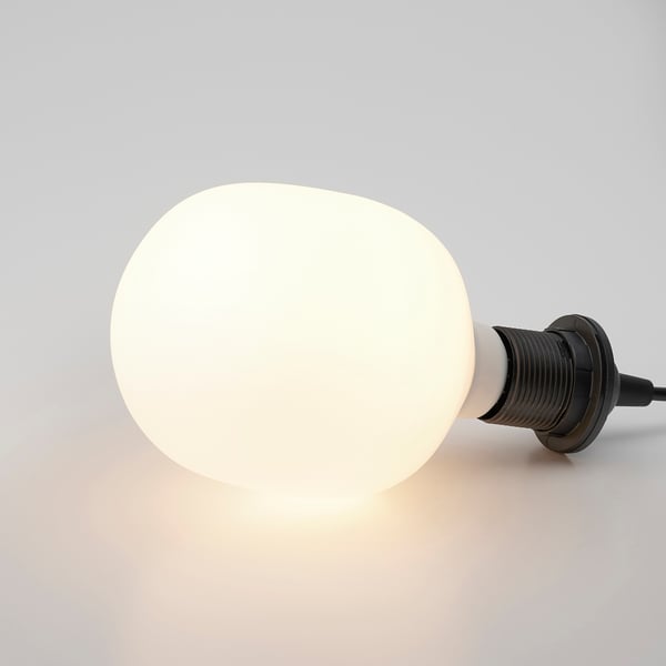 Large frosted light bulb, emitting warm light, with a sleek black base and cable.