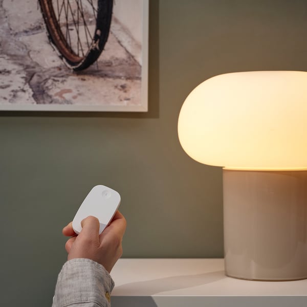 Hand holding remote controls dimmed modern lamp.