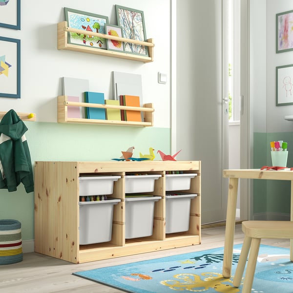 Kids room with TROFAST light wood storage, holding white bins & colourful books, under wall shelves displaying art.