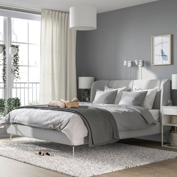 Modern bedroom with TUFJORD bed, rug, nightstands, and plants. Beige curtains frame large window.