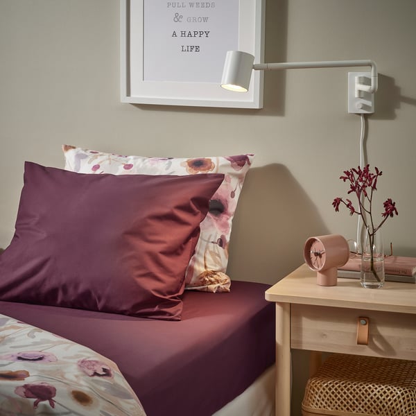Bed with purple sheets, floral pillow, wall clock, vase of flowers, framed quote, ULLVIDE pillowcase.