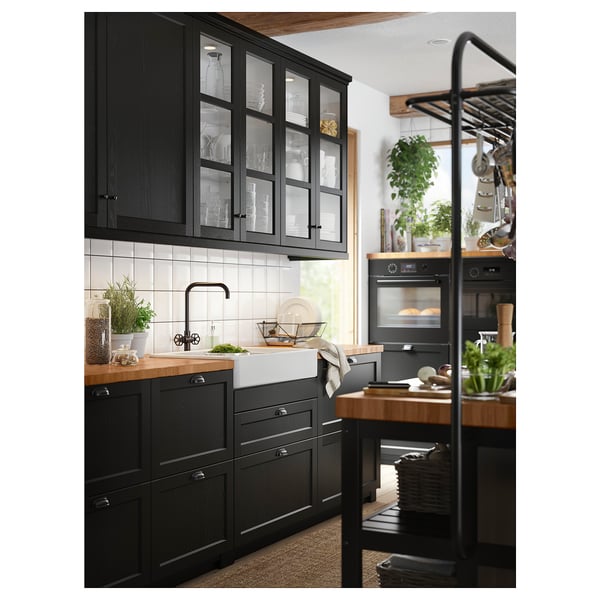 Modern kitchen with black VADHOLMA cabinets, wooden countertops, white sink, and glass-fronted upper cabinets displaying dishes.
