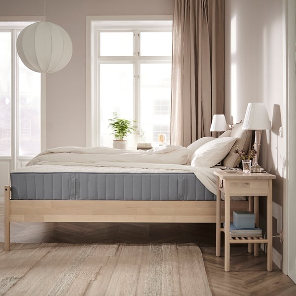 Neutral-toned bedroom with VÅGSTRANDA mattress, side table with lamp & plant, pendant light.