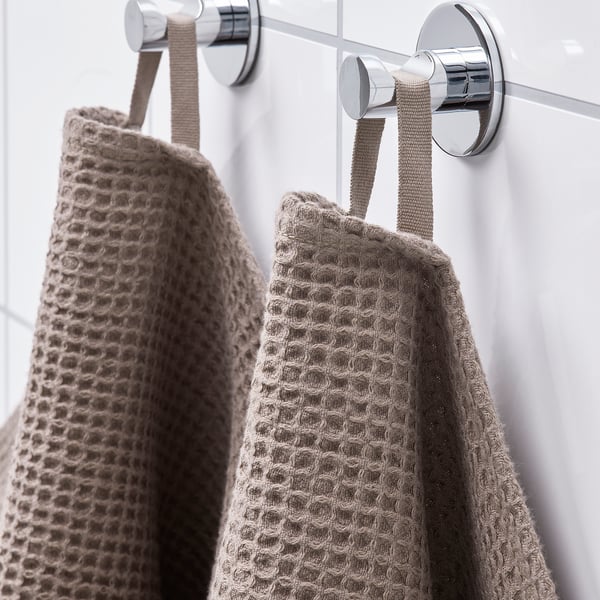 Two light grey towels hang from chrome hooks, showing absorbent, quick-drying material with fringe edging.