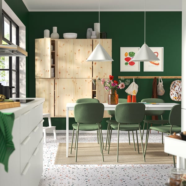 Modern green dining area with extendable table, chairs, natural light, and white lamps. Wooden units and decor enhance eco-friendly design.