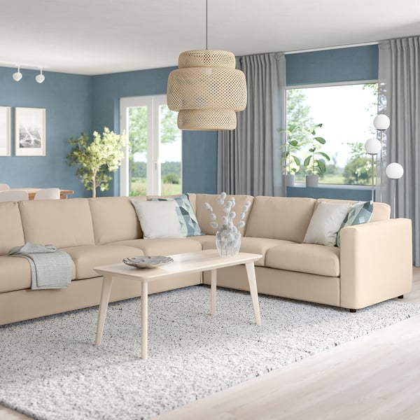 Cosy VIMLE living room with beige sofa, coffee table, and pendant light. Plants, lamp by windows with grey curtains, neutral rug.