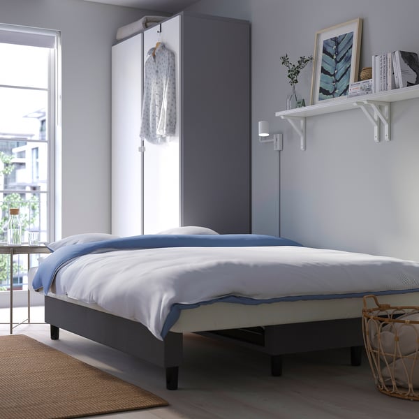 Modernes Schlafzimmer mit blauer Bettwäsche, Bilderrahmen und Tageslicht.
