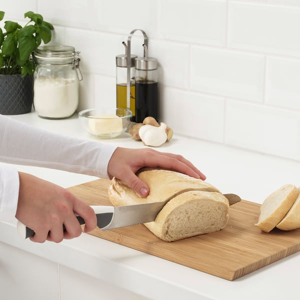 Person schneidet Brot mit Messer auf Schneidebrett in der Küche.