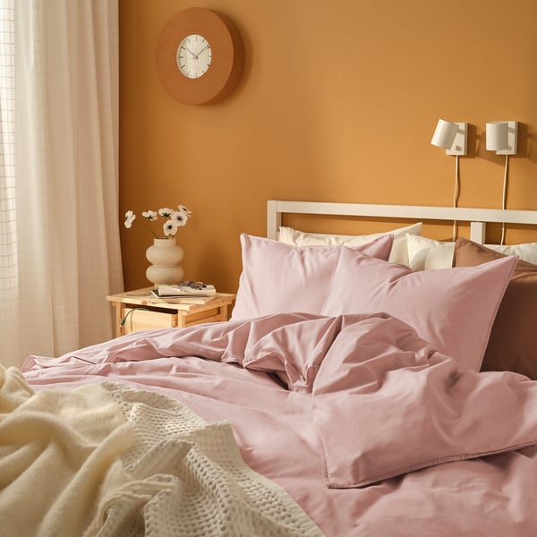 Gemütliches Schlafzimmer mit großer Uhr, rosa Bett, Lampen und Boho-Dekoration.