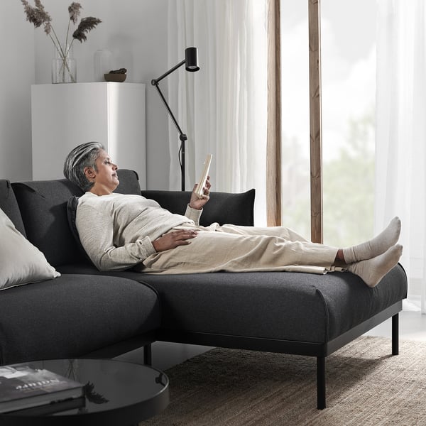 Person mit Smartphone auf modernem ÄPPLARYD Sofa in der Nähe des Fensters.