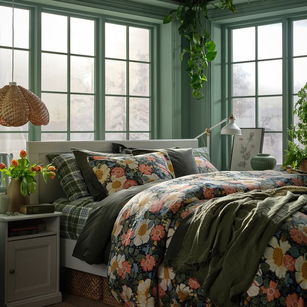 Gemütliches Schlafzimmer mit ARENBOK-Blumenbett, Pendellampe, grün getönten Fenstern und Blumen am Bett.