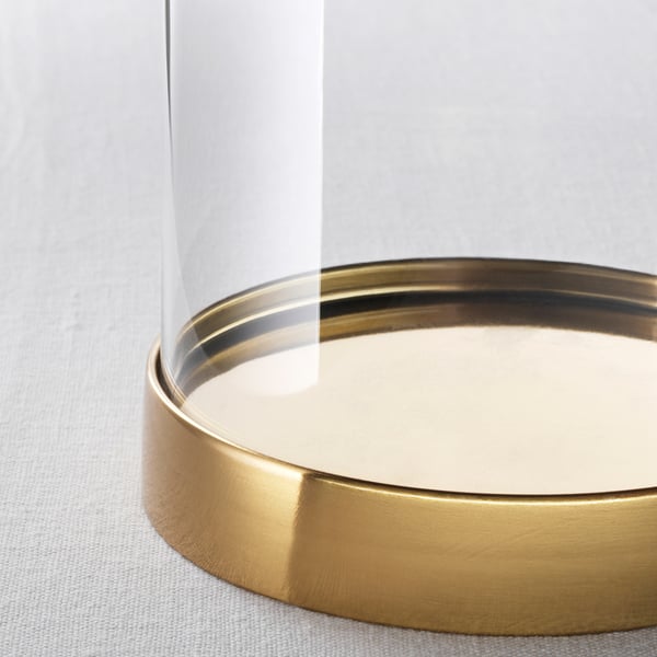 Nahaufnahme einer schlanken, klaren Glaskuppel mit goldenem Metallsockel, die Licht reflektiert und einen dekorativen Gegenstand im Inneren zeigt.
