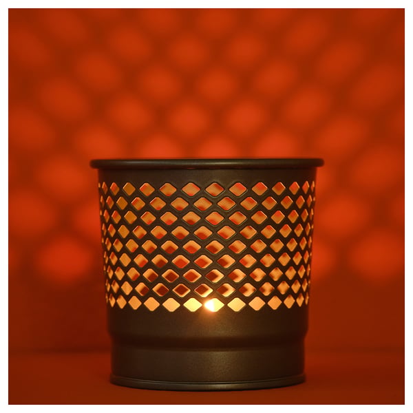 Schwarzer Kerzenhalter mit Diamantausschnitten. Licht scheint warm durch Metall.