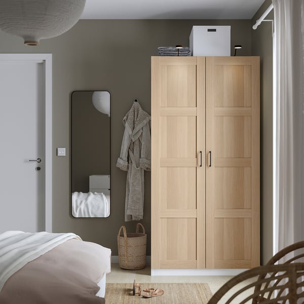 Minimalistisches Schlafzimmer mit BERGSBO-Kleiderschrank, Spiegel, Pendelleuchte und Weidenkorb.