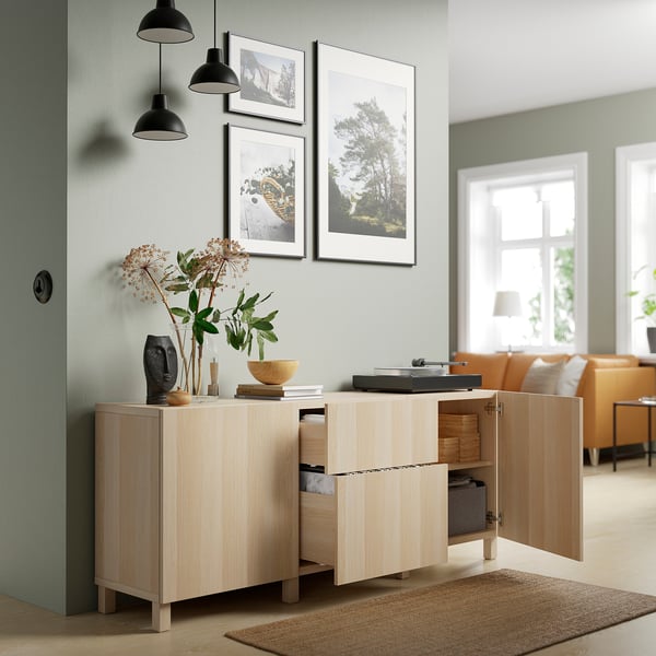 Sideboard aus Holz mit offenen Schubladen, in dem Gegenstände, Bücher und Pflanzen ausgestellt sind. Kunst und Pendelleuchten oben.