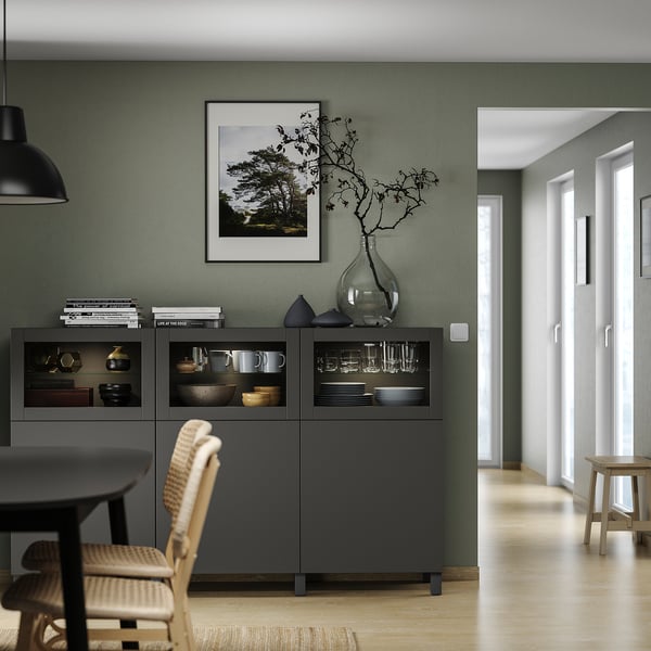 Modernes Wohnzimmer mit grauen BESTÅ-Einheiten, Holzböden, grünen Wänden, schwarzer Pendelleuchte und Glasvitrine.