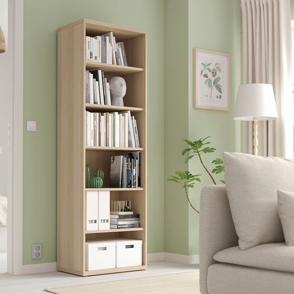 BESTÅ Bücherregal aus Holz mit Büchern und Dekor, höher als Stuhl und Lampe.