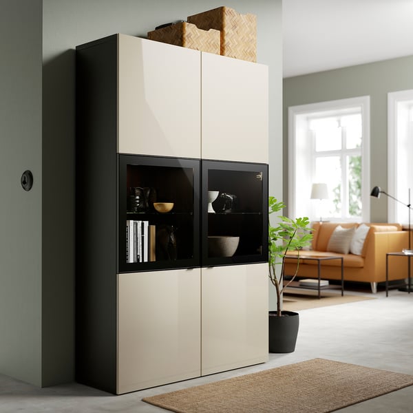 Modernes Wohnzimmer mit BESTÅ-Schrank, Dekor, Glastüren, Regalen, Weidenkorb, orangefarbenem Sofa und Pflanze.