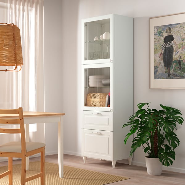 Weißer BESTÅ-Glastürschrank in der Ecke, in der Nähe von Esstisch und Pflanze.