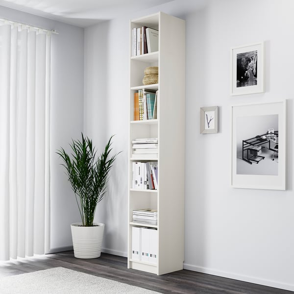 Minimalistisches Zimmer mit weißem Bücherregal BILLY, hoher Pflanze und Wandkunst.