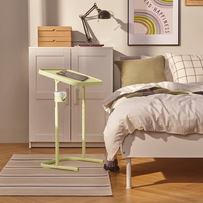 Kleiner grüner Laptop-Stand neben dem Bett, hält das Tablet in der Hand, in verstellbarer Höhe.