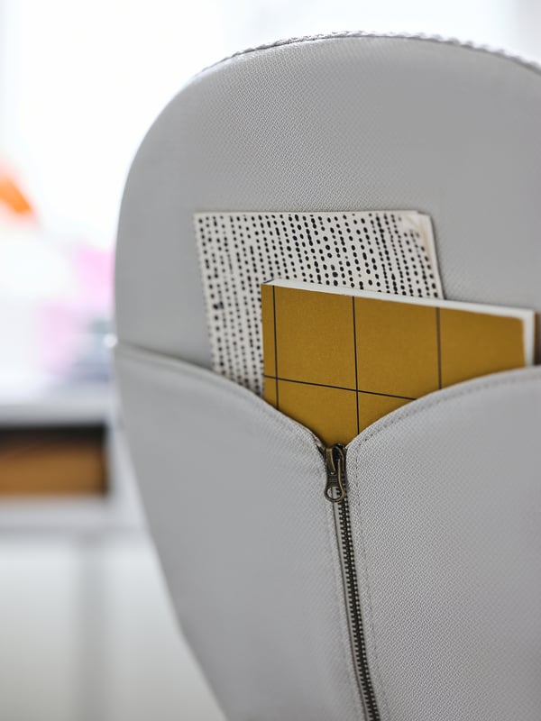 Grauer BJÖRKBERGET-Stuhl mit gelbem Notizblock in der Tasche. Modernes, schlankes Design.