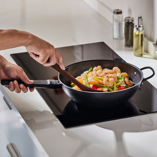 Die Person kocht Garnelen und Gemüsepfannen im BLÅGYLTA-Wok . Die Woks-Antihaftbeschichtung sorgt für eine gleichmäßige Wärmeverteilung und eine einfache Reinigung.