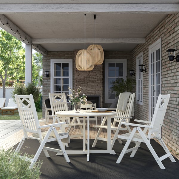 BONDHOLMEN Tisch & Stühle für den Außenbereich, weiß, Akazienholz, rund, mit Kissen, mittig unter einer überdachten Terrasse positioniert.