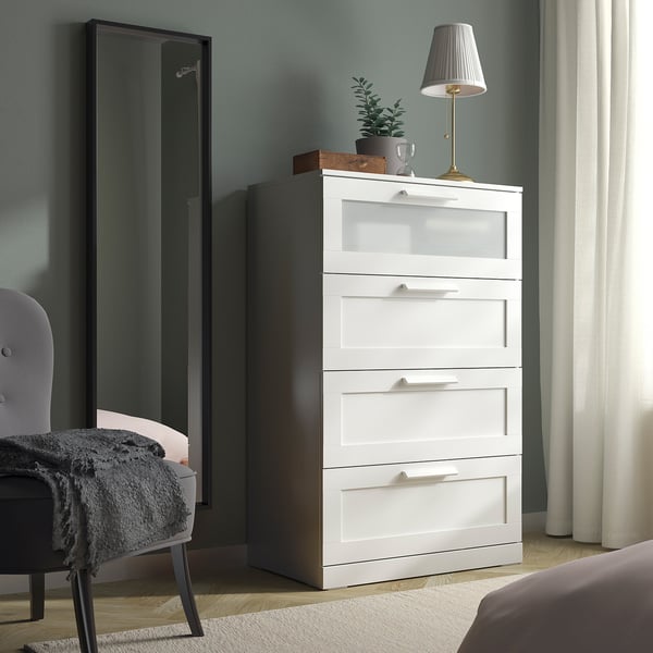 Weiße BRIMNES-Truhe mit Glasplatte, zwischen Spiegel und Bett, moderne Schlafzimmereinrichtung.