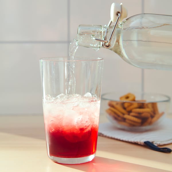 Das durchsichtige Glas gießt Flüssigkeit in ein Glas mit rotem Getränk, neben Brezeln.
