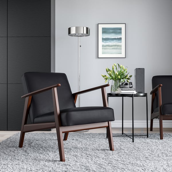 Minimalistisches Wohnzimmer mit 2 schwarzen EKENÄSET-Stühlen, Beistelltisch, Blumen, Büchern und Wandkunst.
