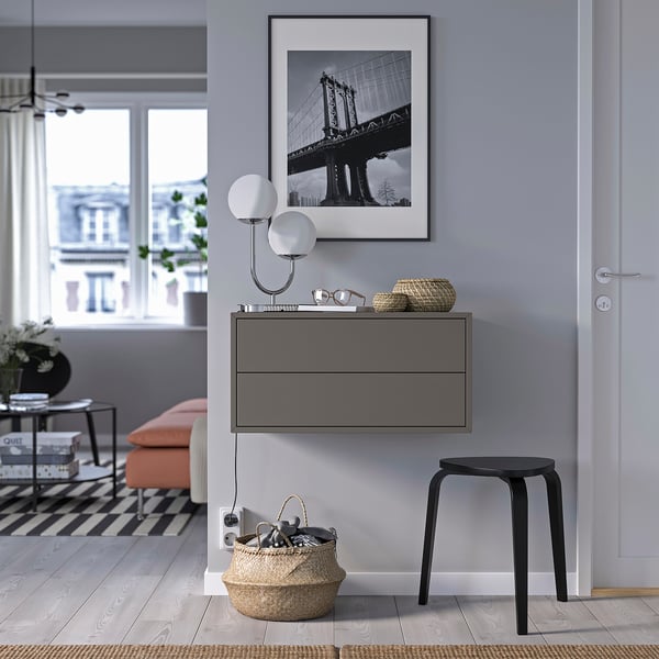 Modernes Zimmer: schwarz gerahmte Brückenkunst, Wandlampe, grauer Schrank mit Schubladen, orangefarbene Bank, schwarzer Hocker, großer Korb mit Schlüsseln.