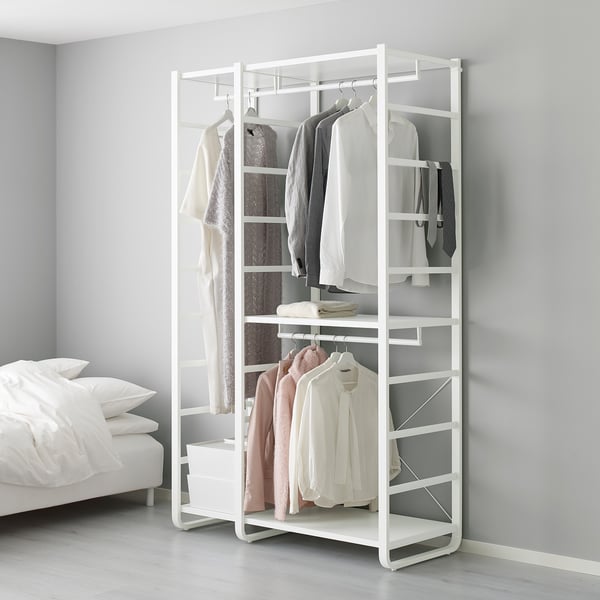 Weißer ELVARLI Kleiderständer mit hängenden Kleidungsstücken und Regalen neben dem Bett.