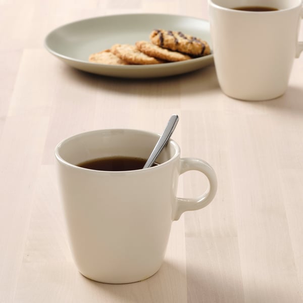 Zwei weiße Tassen gefüllt mit Kaffee, eine mit einem Löffel und ein Teller mit Keksen.
