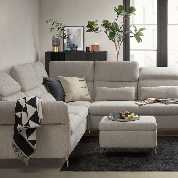 Modernes Wohnzimmer mit einem grauen FAMMARP-Sofa mit Kissen, einem Fußhocker und Dekorationsgegenständen.